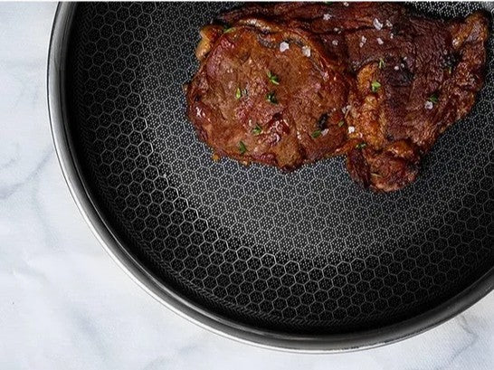 Ostrera 28 cm stainless steel hybrid frying pan with a honeycomb non-stick surface searing a cooked steak